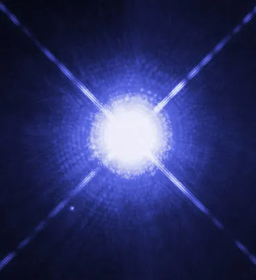 A brilliant white star with diffraction spikes fills the frame; a tiny faint dot sits to its lower left.