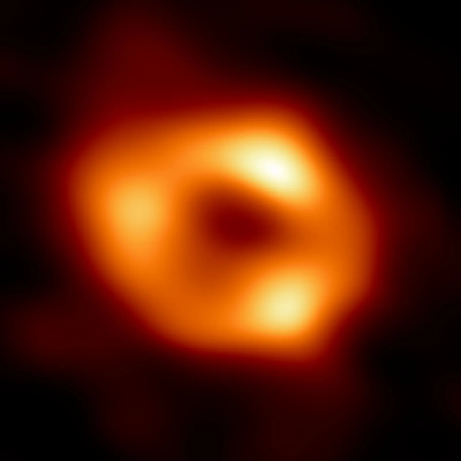 A blurred orange ring of light with three brighter knots around a dark centre, on a black background.
