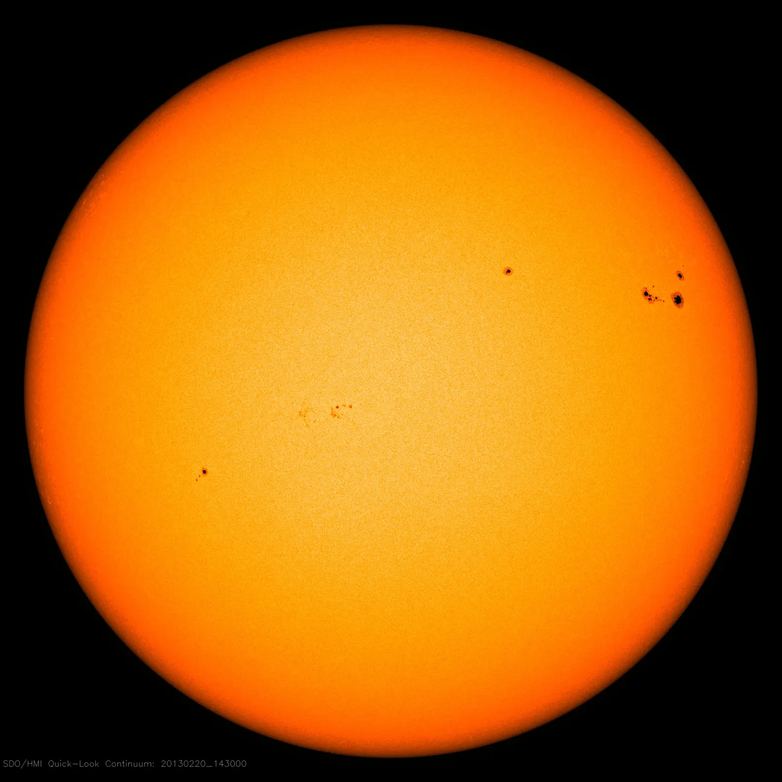 The Sun's full disc in visible light, bright at the centre and darker toward the edge, with a few small dark sunspot groups