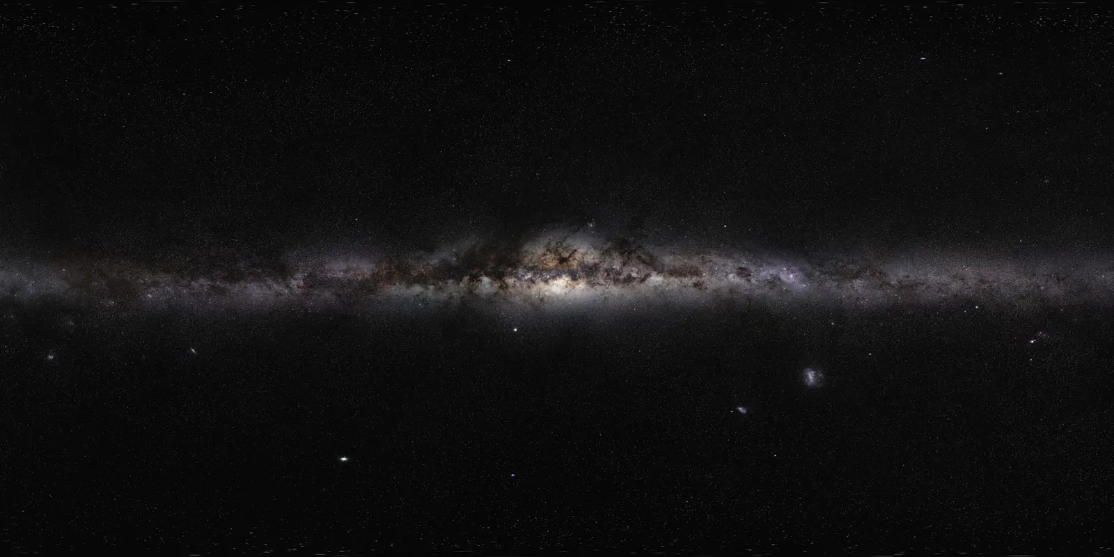 A long panoramic photograph of the whole Milky Way as a glowing band across a dark sky, dark dust lanes running through it and the bright central bulge in the middle